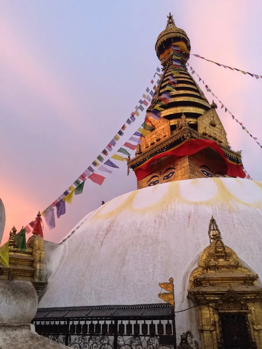 The stupa and its prayer flags against a pink evening sky